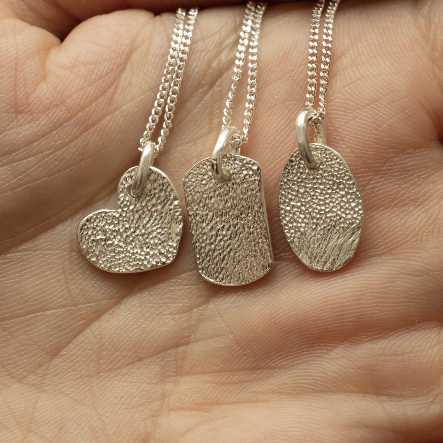 signet "CHARM" mini silver fingerprint jewelry in heart, tag, and oval shapes on a hand.